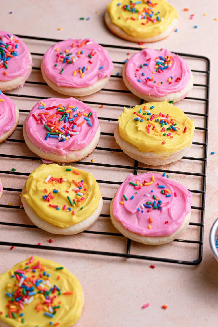 Yellow and pink frosted Lofthouse cookies on a cooling rack.