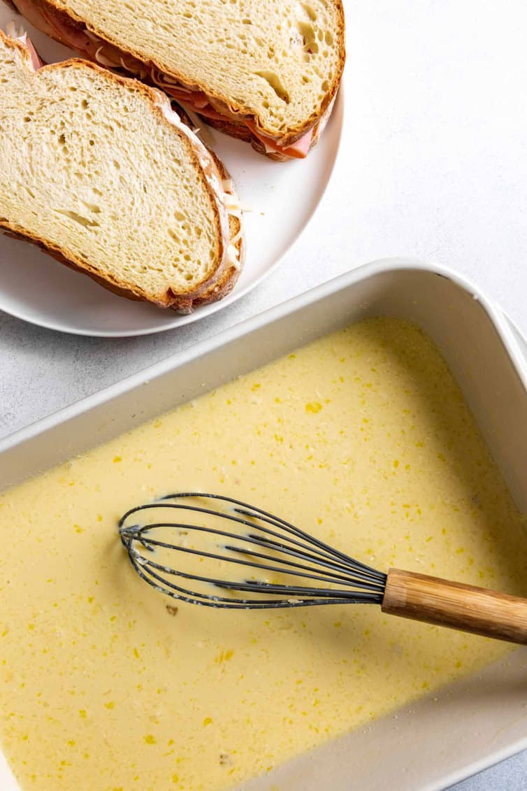 Pan of custard with a whisk and a plate with slices of bread.