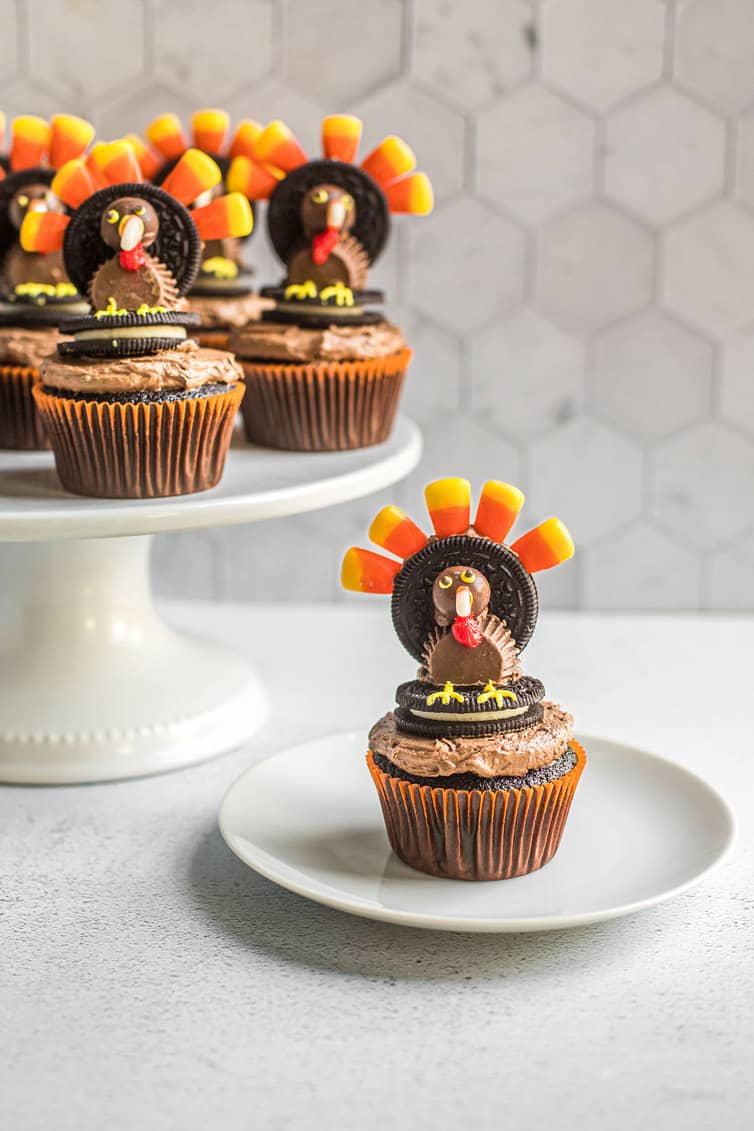 Turkey cupcake on white plate with others on cake pedastal behind.