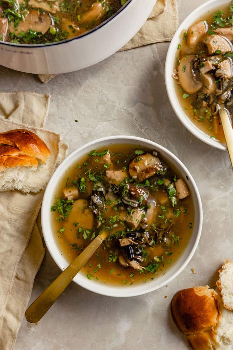 A bowl of turkey wild rice soup with bread and rolls on the side.
