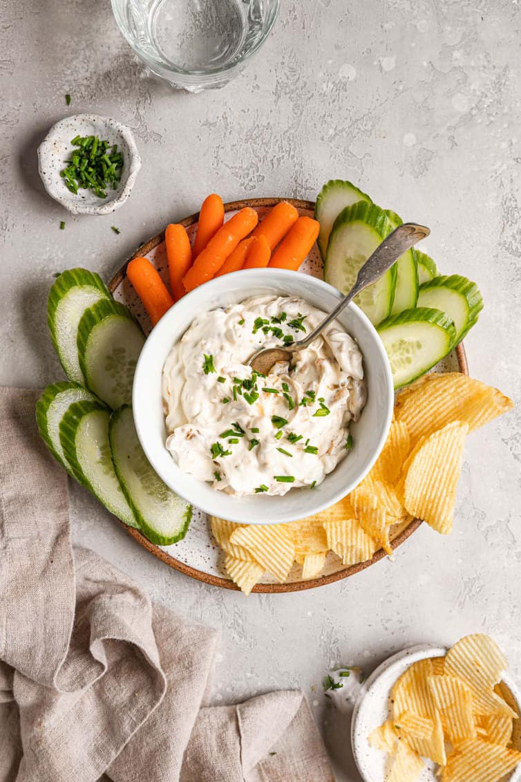 Homemade French onion dip surrounded by sliced vegetables and potato chips.