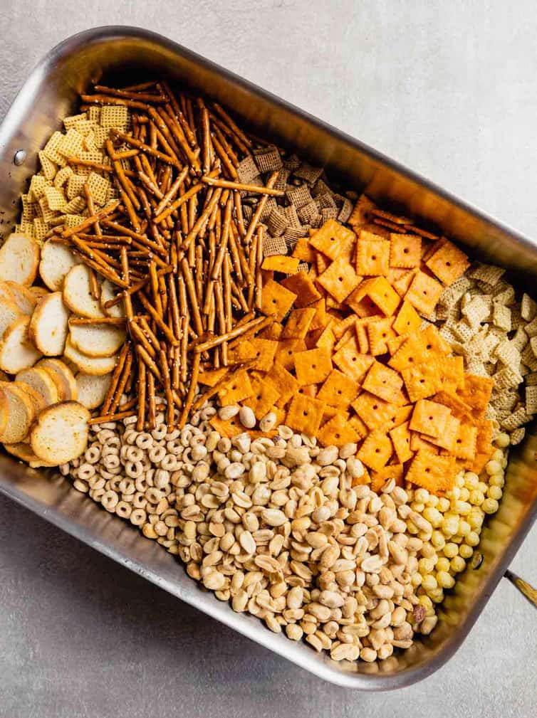Roasting pan filled with pretzel sticks, Cheezits, Cheerios, bagel chips, Chex cereals, and peanuts.