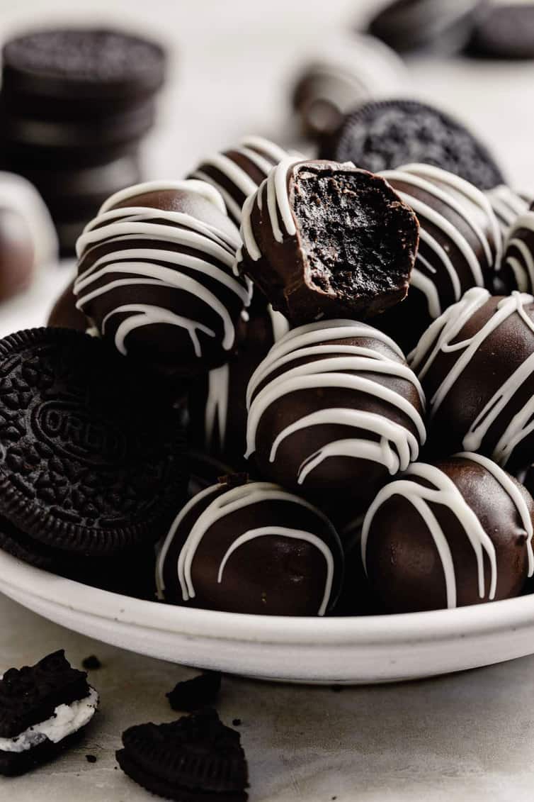A pile of Oreo truffles on a plate with one bitten into.