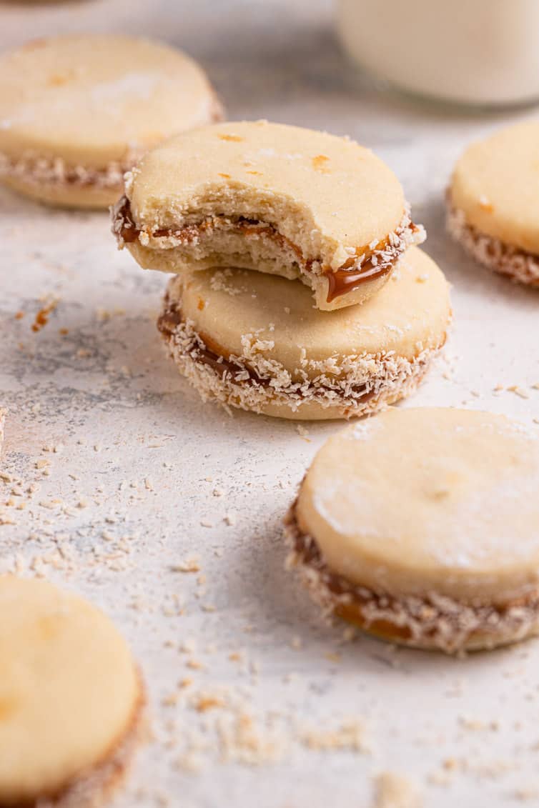 One alfajor stacked on another with a bite taken out and other alfajores spread around the stack.