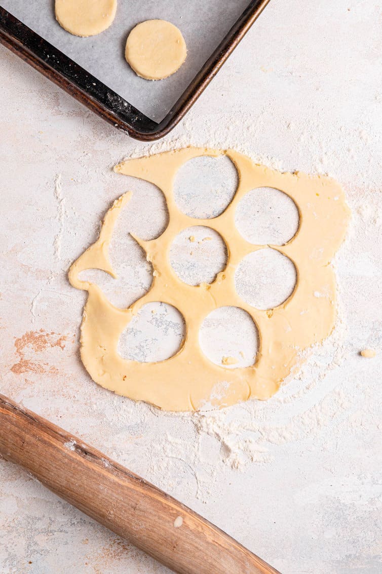 Cookie dough with cut out pieces, a rolling pin in the bottom left and a baking sheet lined with parchment paper in the top.