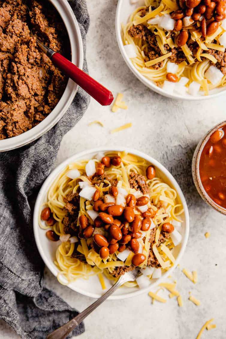 Overhead photo of plates piled high with Cincinnati chili and toppings.