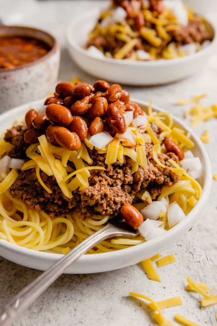 A plate of spaghetti topped with Cincinnati chili, shredded cheese, onion, and beans.