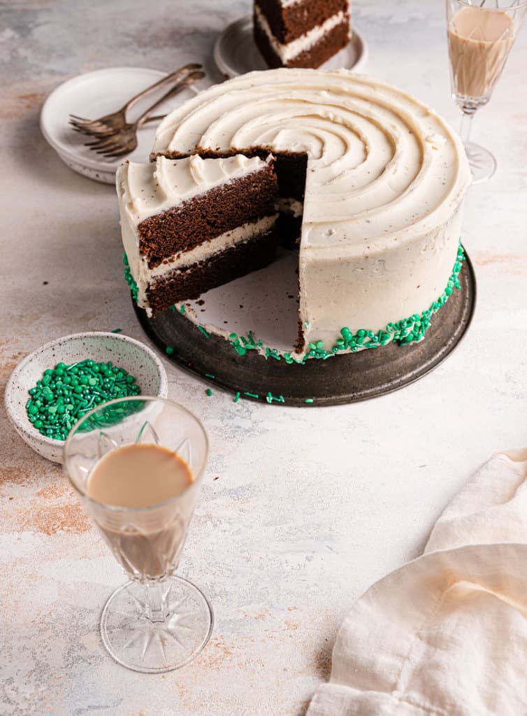 A chocolate guinness cake on a cake stand with a slice taken out behind a glass of baileys.