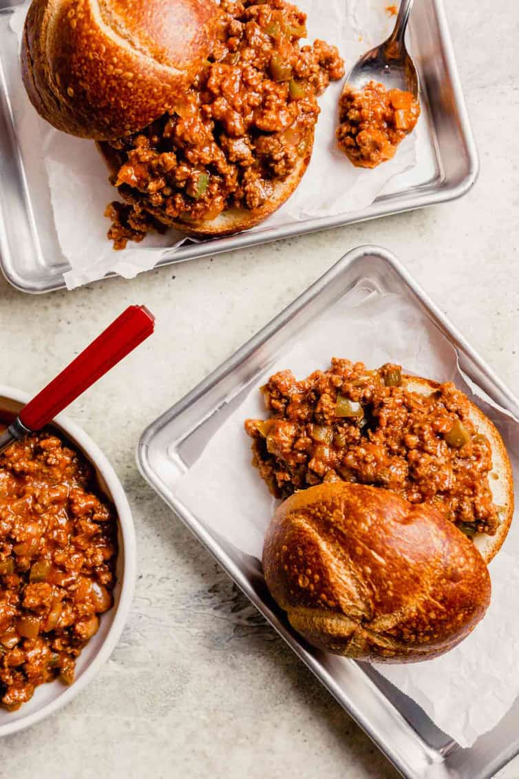 Two metal trays lined with parchment paper with homemade sloppy joes on top of the parchment paper with a small skillet of sloppy joe meat to the left.