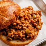 A square photo from the front of a sloppy joe sandwich with the top of the bun slid back to show the sloppy joe meat.