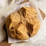 A loaf of Irish Brown Bread on a piece of parchment paper on a wooden cutting board.