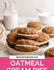 A table set with a white plate of oatmeal cream pies, a small glass of milk in the back left, and a small bowl in the back right with a pink rectangle at the bottom and the words Oatmeal Cream Pies in white.