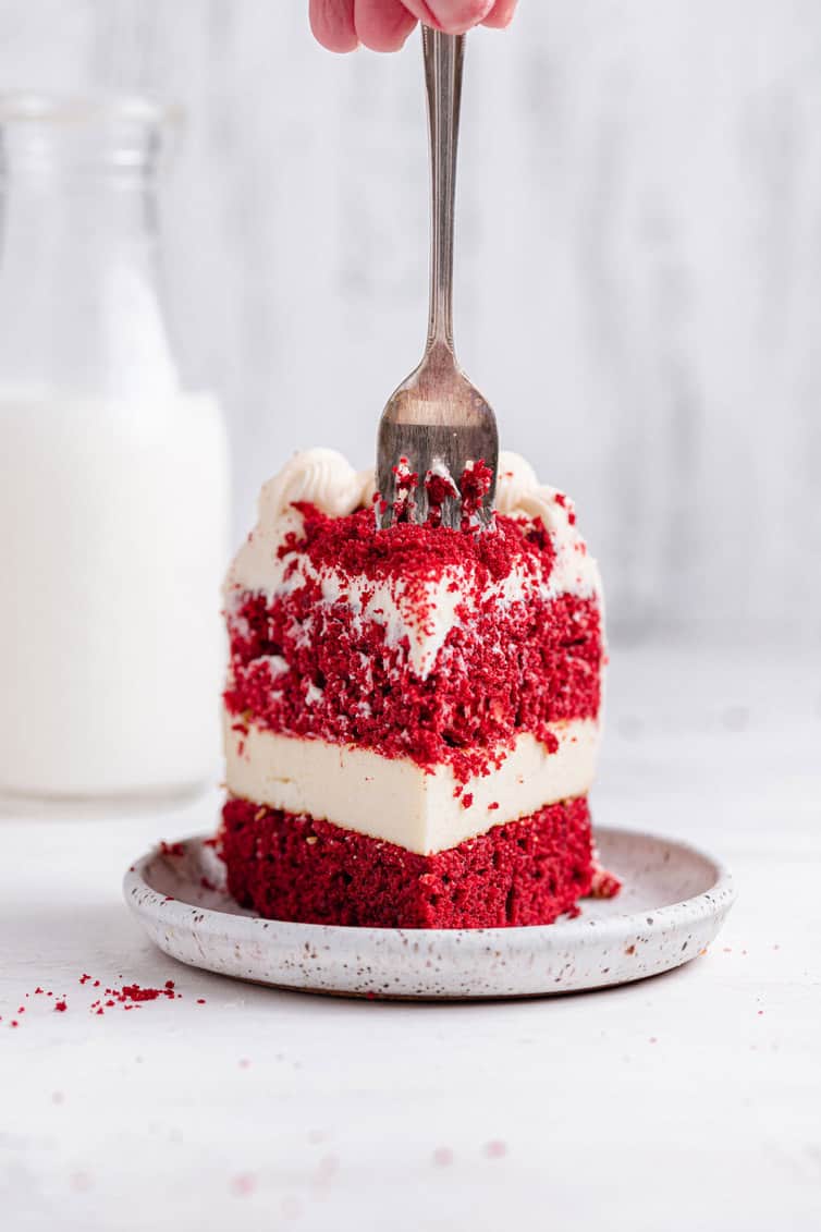 A slice of red velvet cheesecake from the front with a fork in the top.