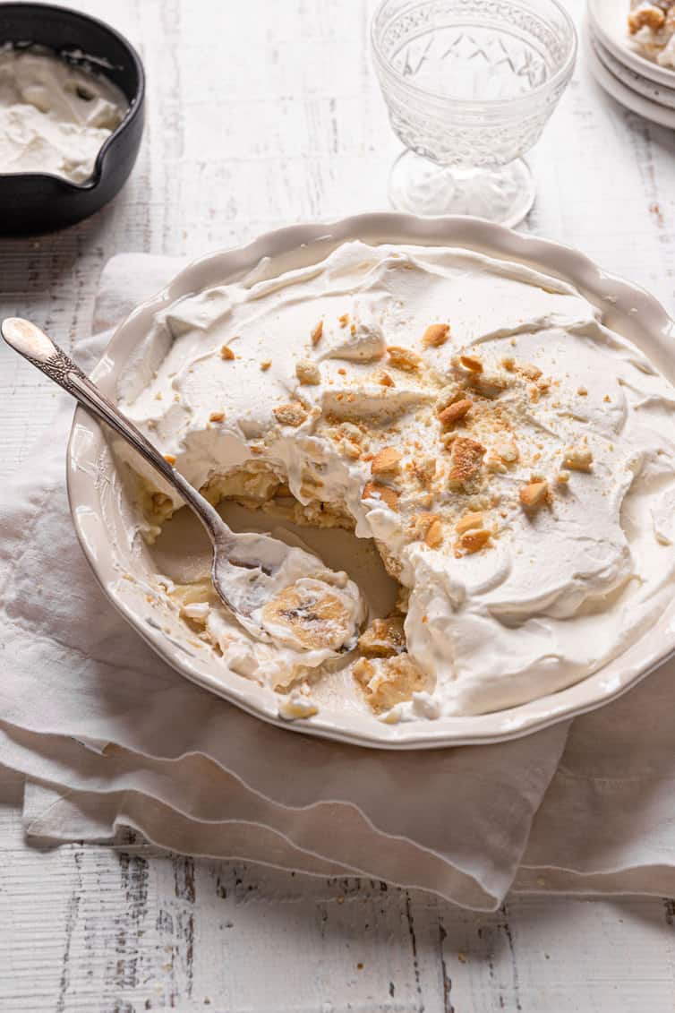 A pie dish of banana pudding with a scoop missing and a sliver spoon in place of the pudding.