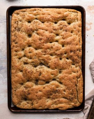 A top down photo of a baking sheet lined with parchment paper and fresh baked focaccia next to a bread knife on the right.
