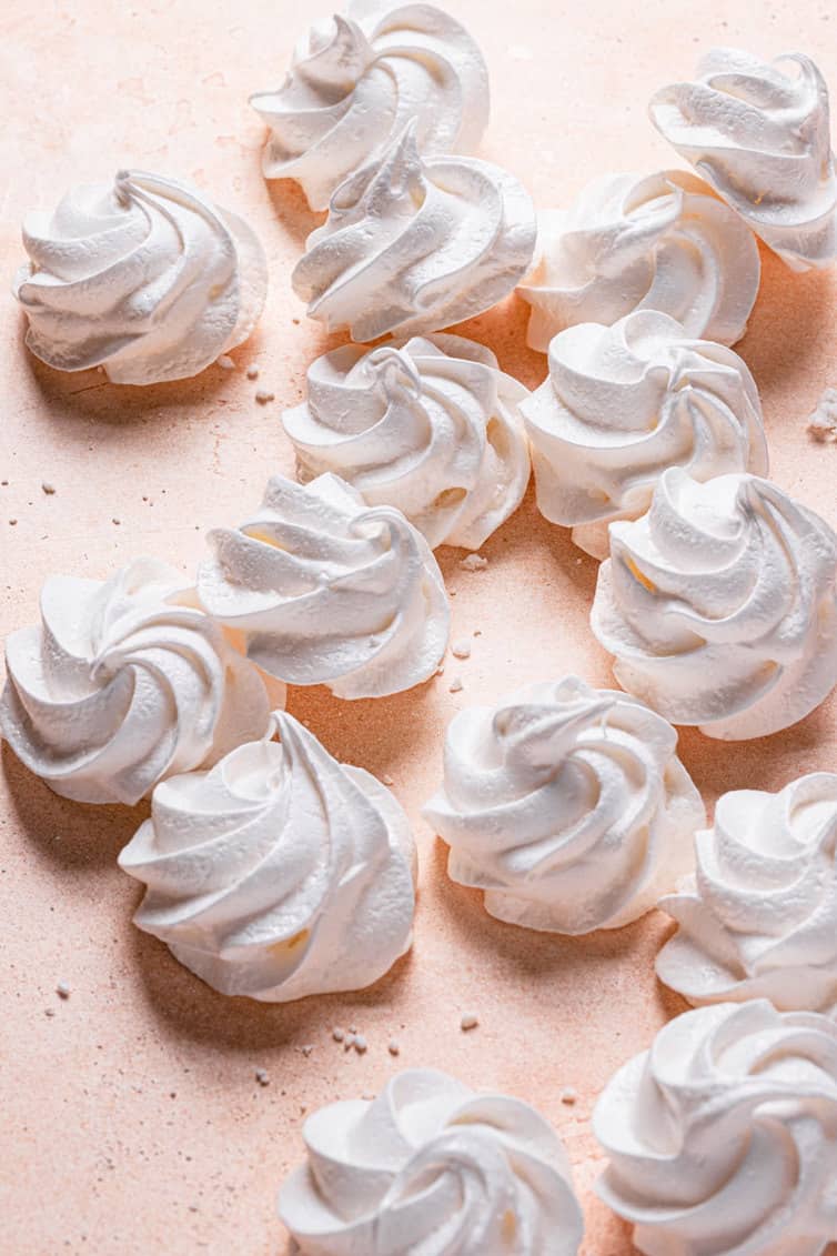 White meringue cookies spread on a pink counter.