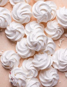 A pile of piped meringue cookies baked and on a pink counter.