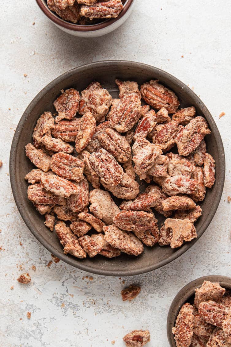 A brown bowl with candied pecans on a white counter with small bowls of candied pecans.