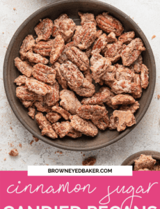 A brown bowl of candied pecans on a white counter with a pink rectangle at the bottom that says cinnamon sugar candied pecans in white.