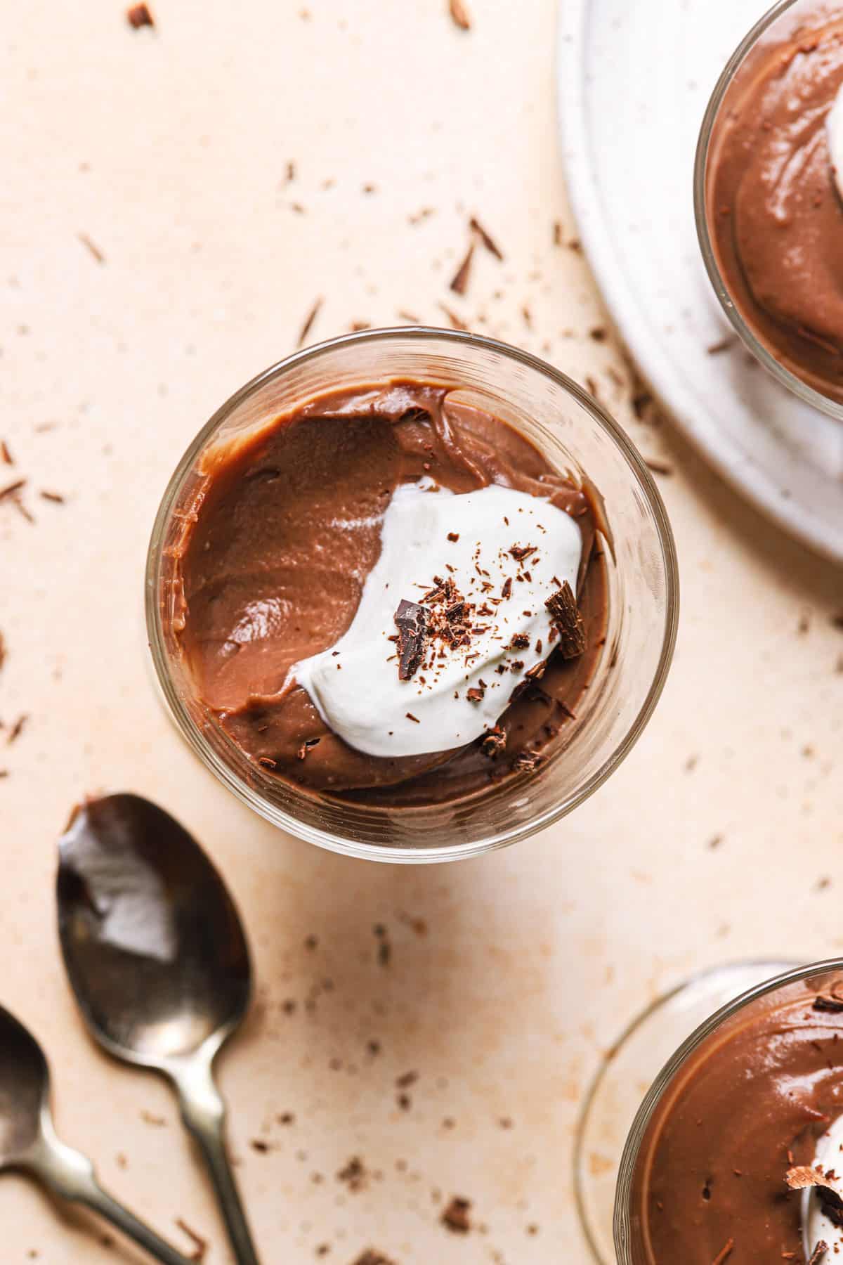 A top down photo of a glass of chocolate pudding with whipped cream and a scoop taken out of the left side of the cup.