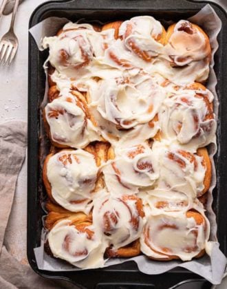 A baking pan with cinnamon rolls covered in cream cheese frosting with a stack of forks in the top left.