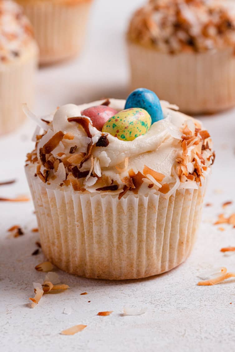 A coconut cupcake with the cupcake liner topped with toasted coconut and eggs on a white counter.