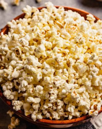 A brown bowl with fresh, homemade popcorn and some pieces of popcorn scattered on the counter.
