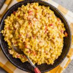 A square photo of Mexican corn salad in a black bowl on a white and yellow towel.