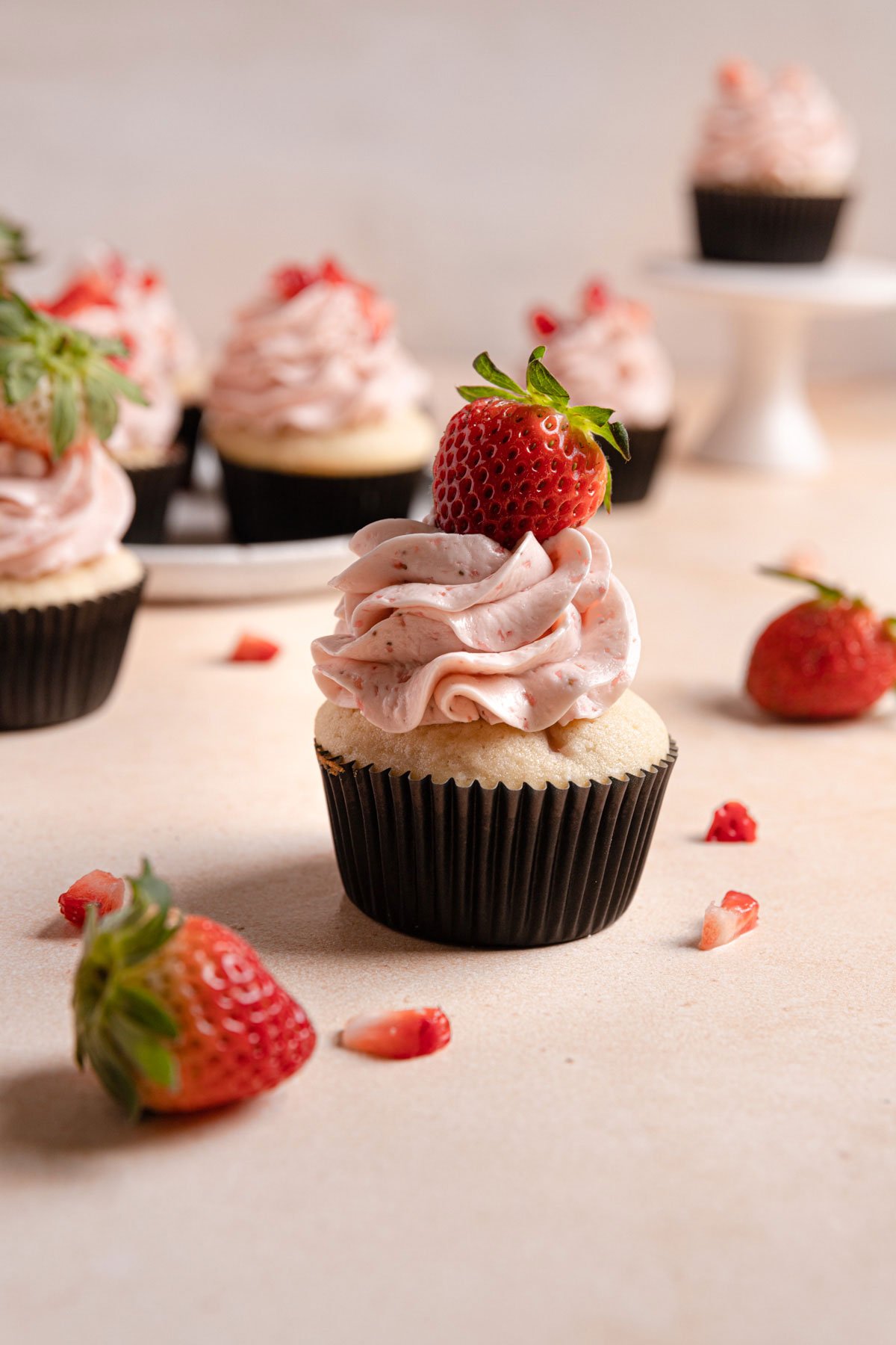 Strawberry cupcakes topped with fresh strawberries on a pink counter.