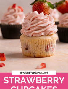 A strawberry cupcake topped with fresh strawberry frosting on a pink counter with a pink box at the bottom with the words strawberry cupcakes in white.
