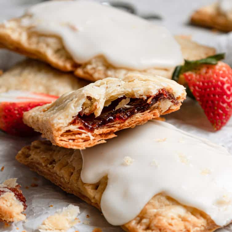 Half of a strawberry pop tart on top of iced homemade pop tarts on a piece of parchment paper.