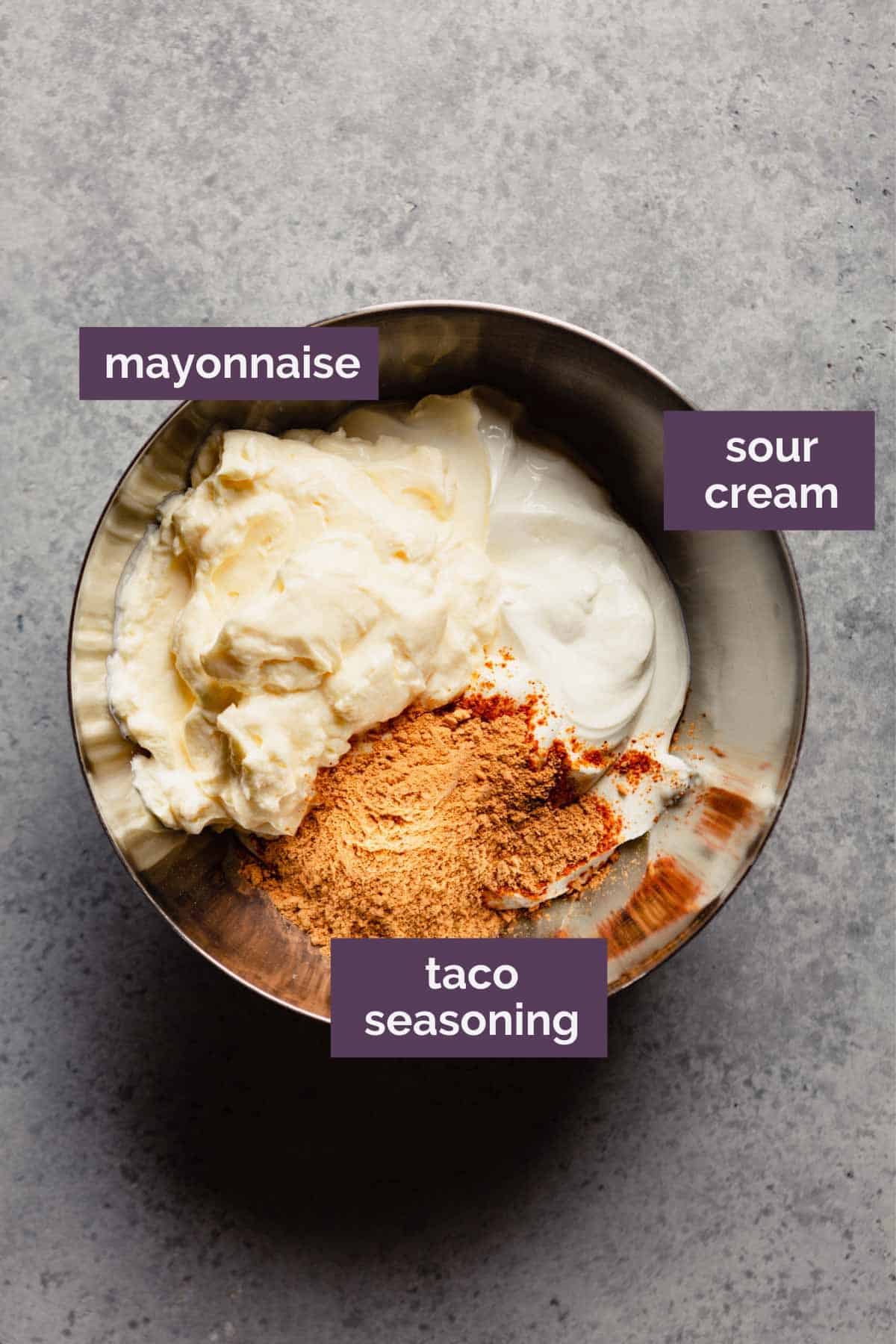 A silver mixing bowl with the ingredients for taco dip filling with labels in purple.