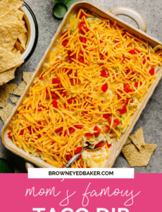 A top down photo of taco dip topped with cheese on a counter with tortilla chips around.