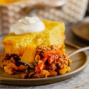 A square photo of tamale pie on a brown plate topped with sour cream.