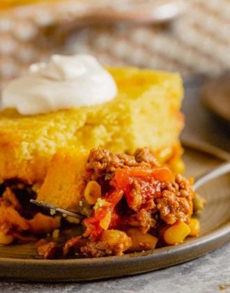A square photo of tamale pie on a brown plate topped with sour cream.