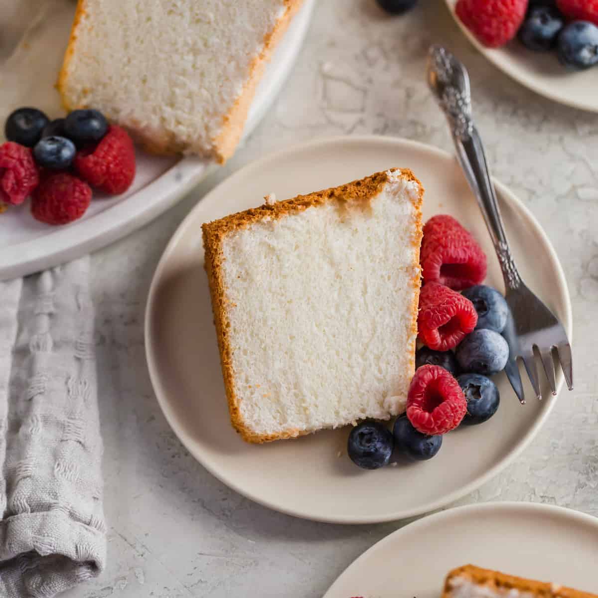 Slice of angel food cake on a plate with raspberries and blueberries.