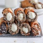 Two rows of homemade cannoli stacked on each other on top of a cooling rack.