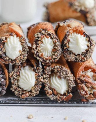 Two rows of homemade cannoli stacked on each other on top of a cooling rack.