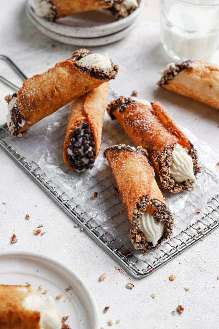 A close up of four cannoli on a wire rack with a cannoli in the back and the rim of a plate in the front left.