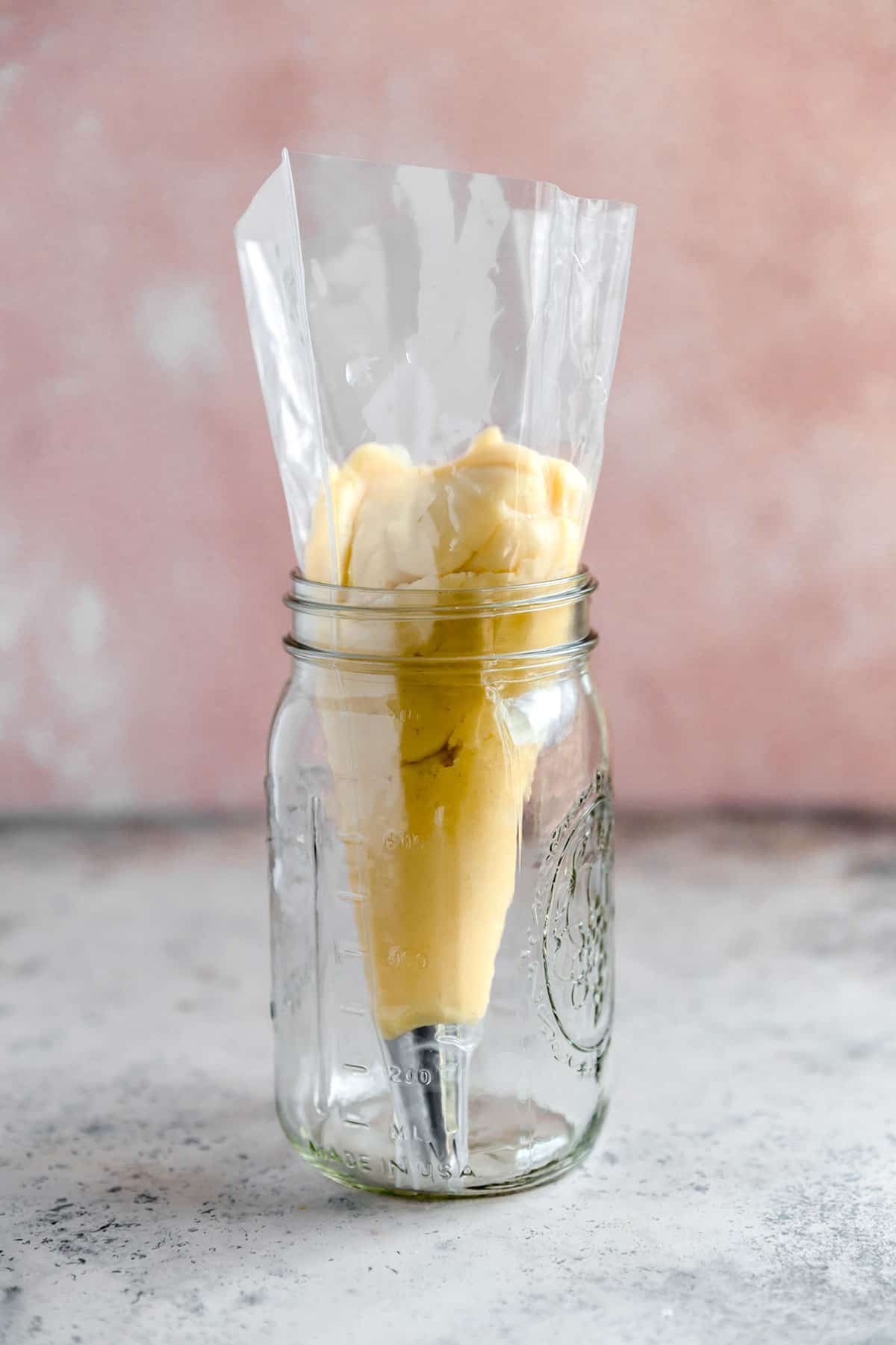 A pastry bag fitted with a star tip and filled with choux pastry in a mason jar to hold it up.