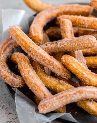 A pie pan lined with parchment paper and topped with fresh fried churros.