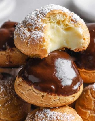 A close up of the top of a tower of cream puffs that has one cream puff on top with a missing bite.
