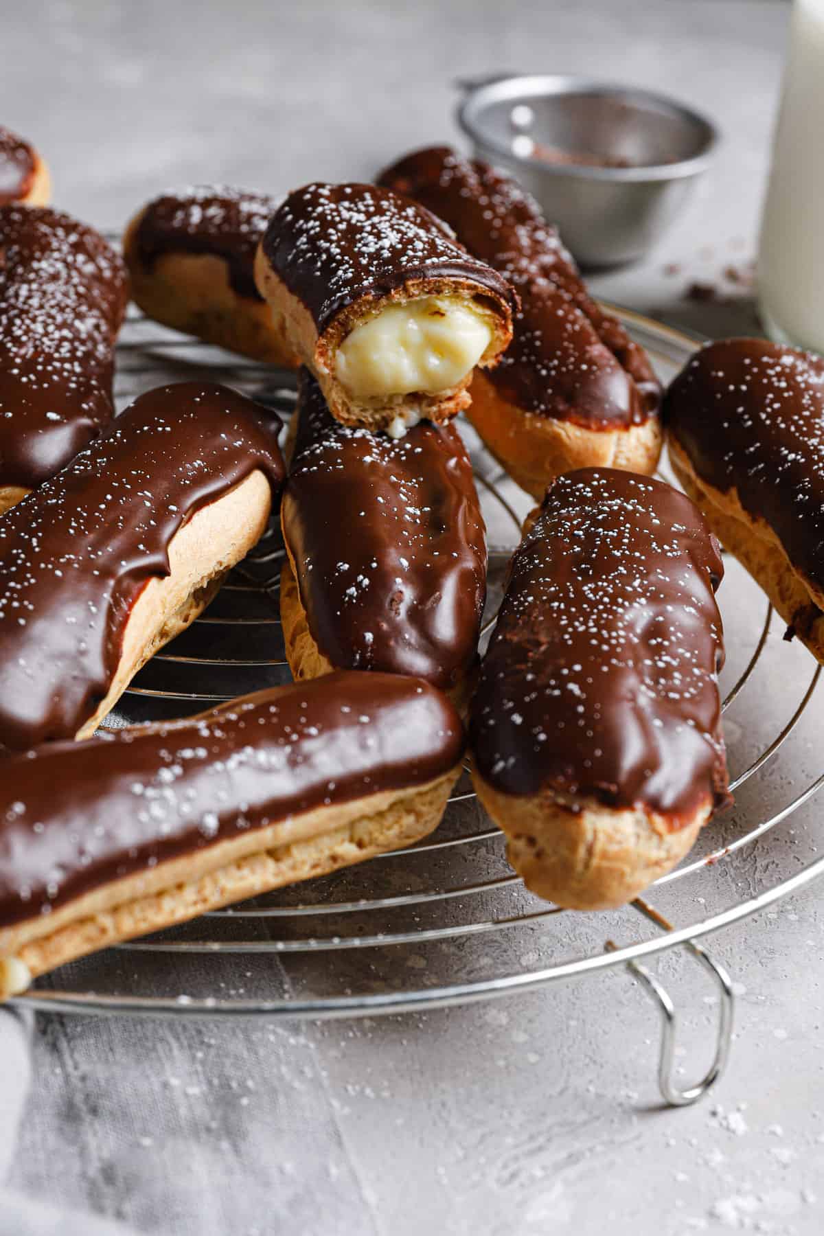 From the side, eclairs cooling on a wire rack with one eclair showing the inside of the pastry.