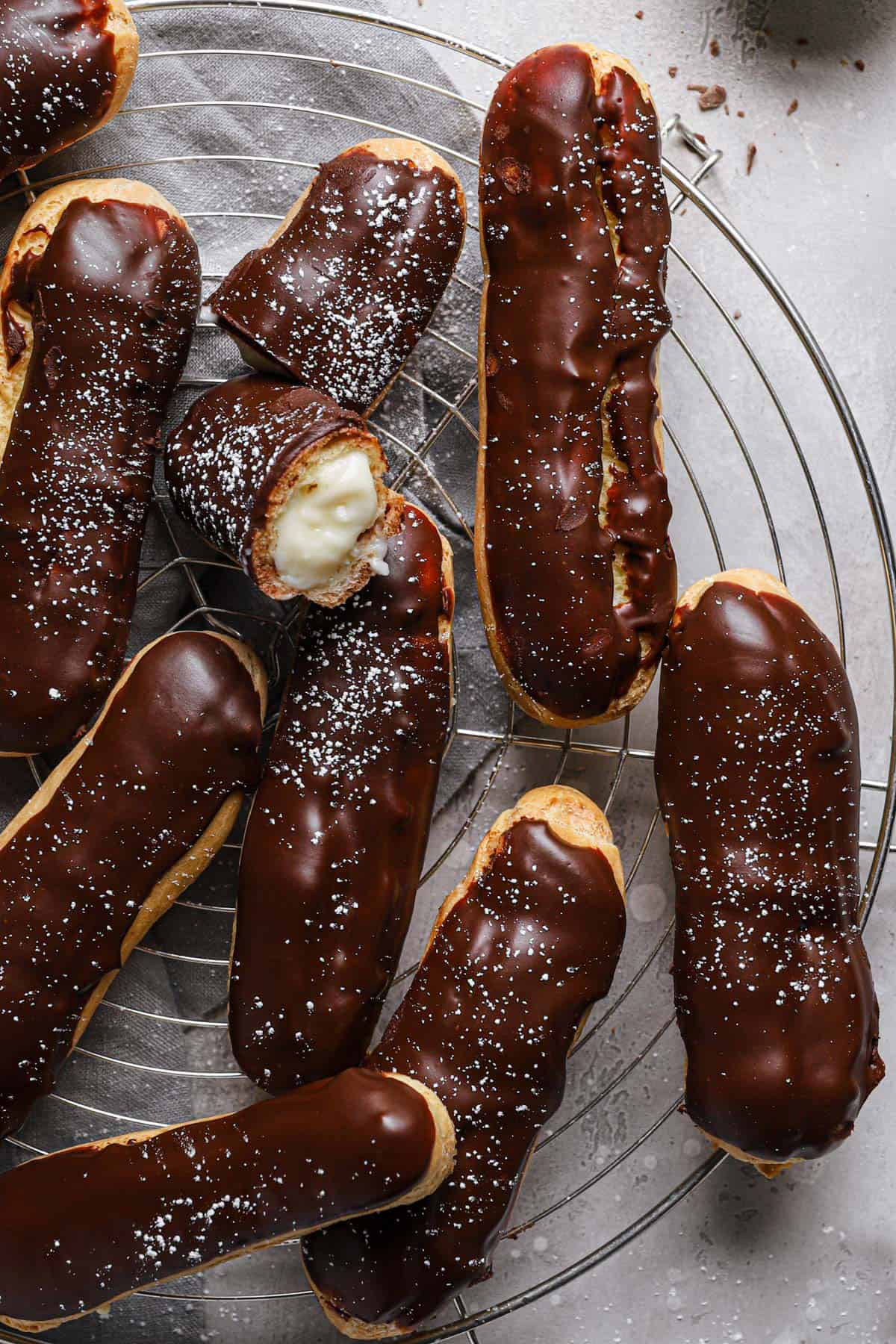 Chocolate dipped eclairs on a cooling rack with a bite taken out of the center eclair.
