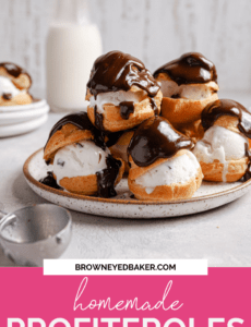 A white plate with a brown rim topped with a tower of vanilla ice cream filled profiteroles topped with chocolate sauce and a jar of milk in the back with a pink rectangle at the bottom and the words homemade profiteroles in white.