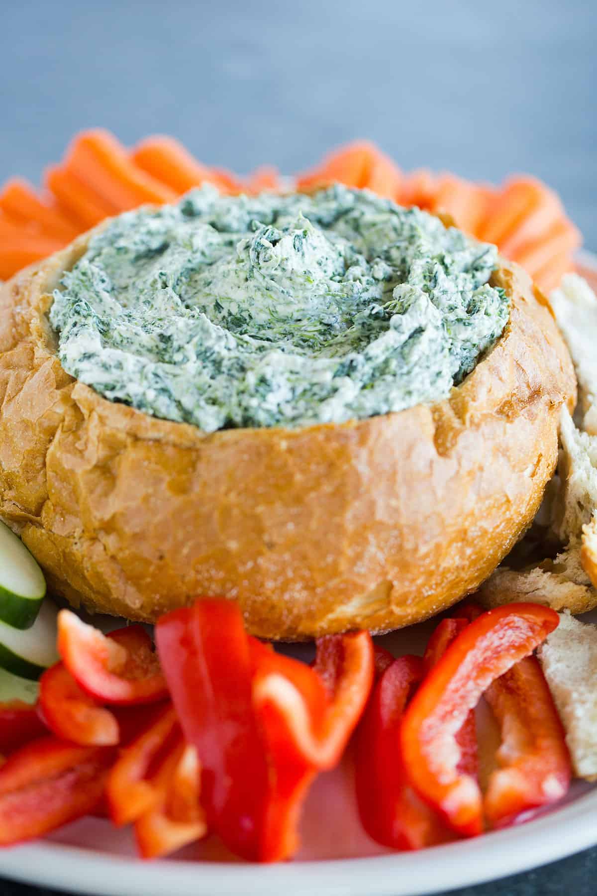 A platter with vegetables around a bread bowl with spinach dip.