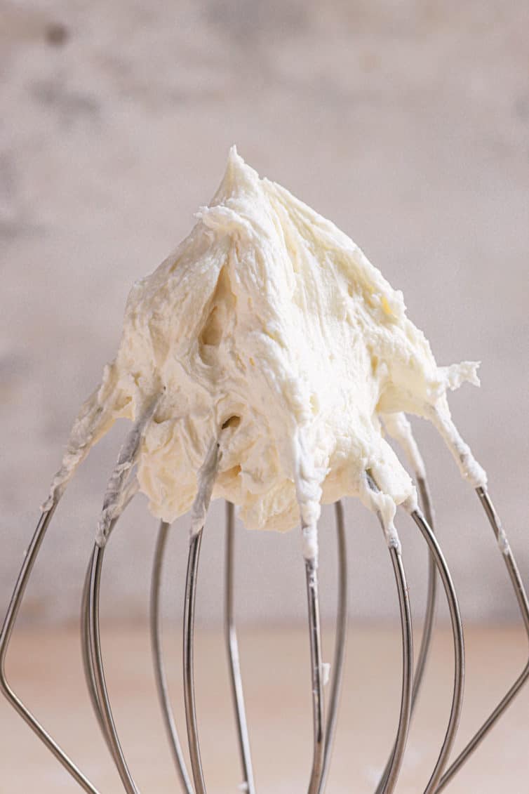 A close up of a wire whisk with vanilla buttercream on the top.