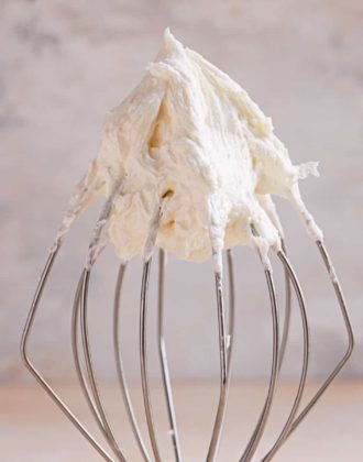 A square photo of vanilla buttercream frosting on a wire whisk.