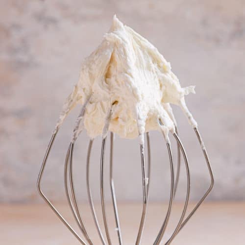 A square photo of vanilla buttercream frosting on a wire whisk.