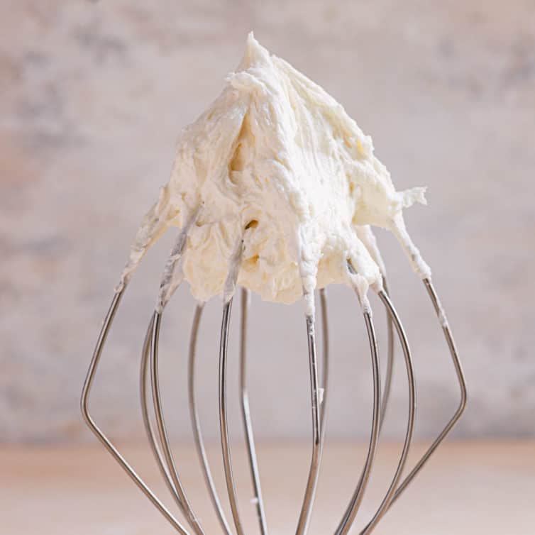 A square photo of vanilla buttercream frosting on a wire whisk.